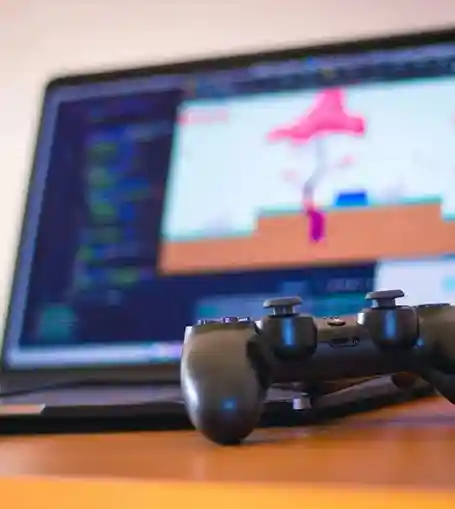 Game controller resting on a desk in front of a laptop with video game development software open